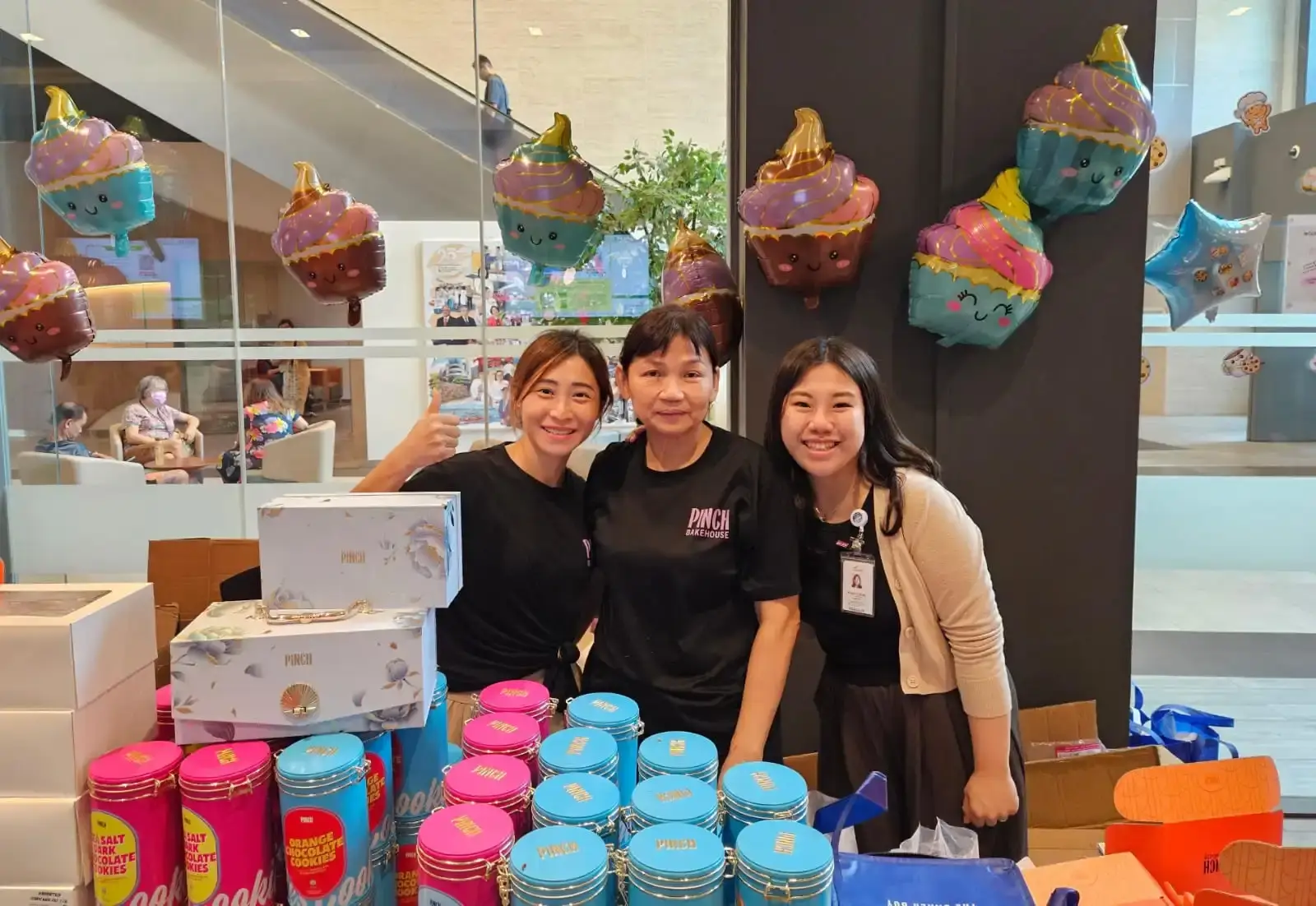 Pinch Bakehouse team and NCCS staff at a charity bake sale booth with halal cookie tins and dessert gift boxes