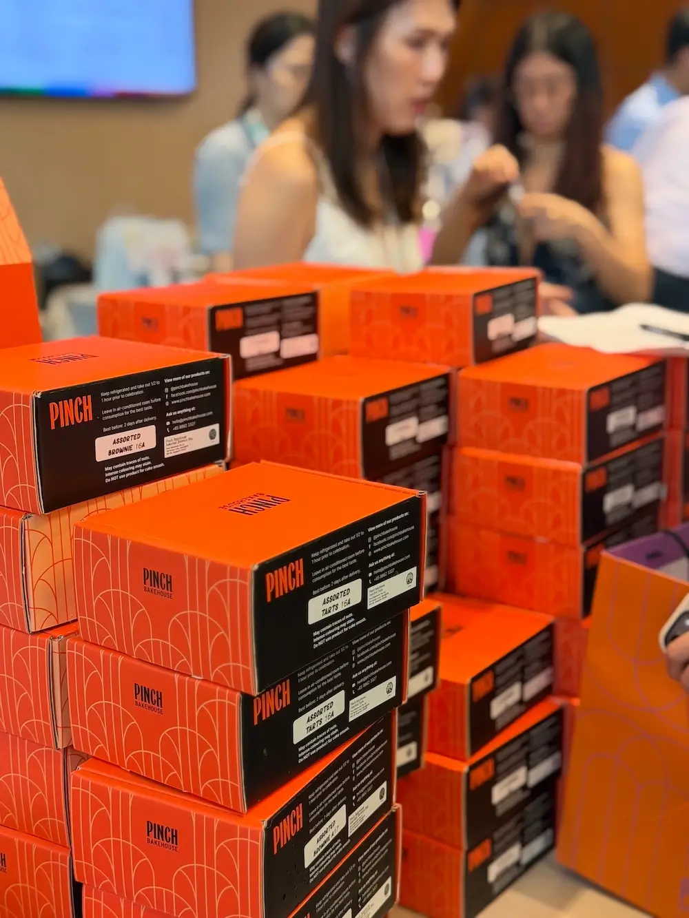 Large stacks of Pinch Bakehouse brownie and tart boxes prepared for the NCCS charity bake sale in Singapore